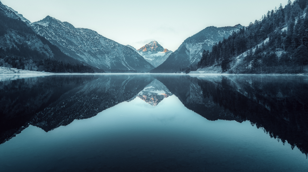 HÖLLBACH Rechtsanwälte Berglandschaft mit spiegelglattem See und schneebedeckten Gipfeln im Hintergrund.