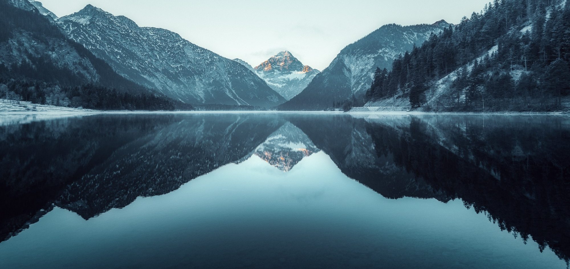 HÖLLBACH Rechtsanwälte Berglandschaft mit spiegelglattem See und schneebedeckten Gipfeln im Hintergrund.